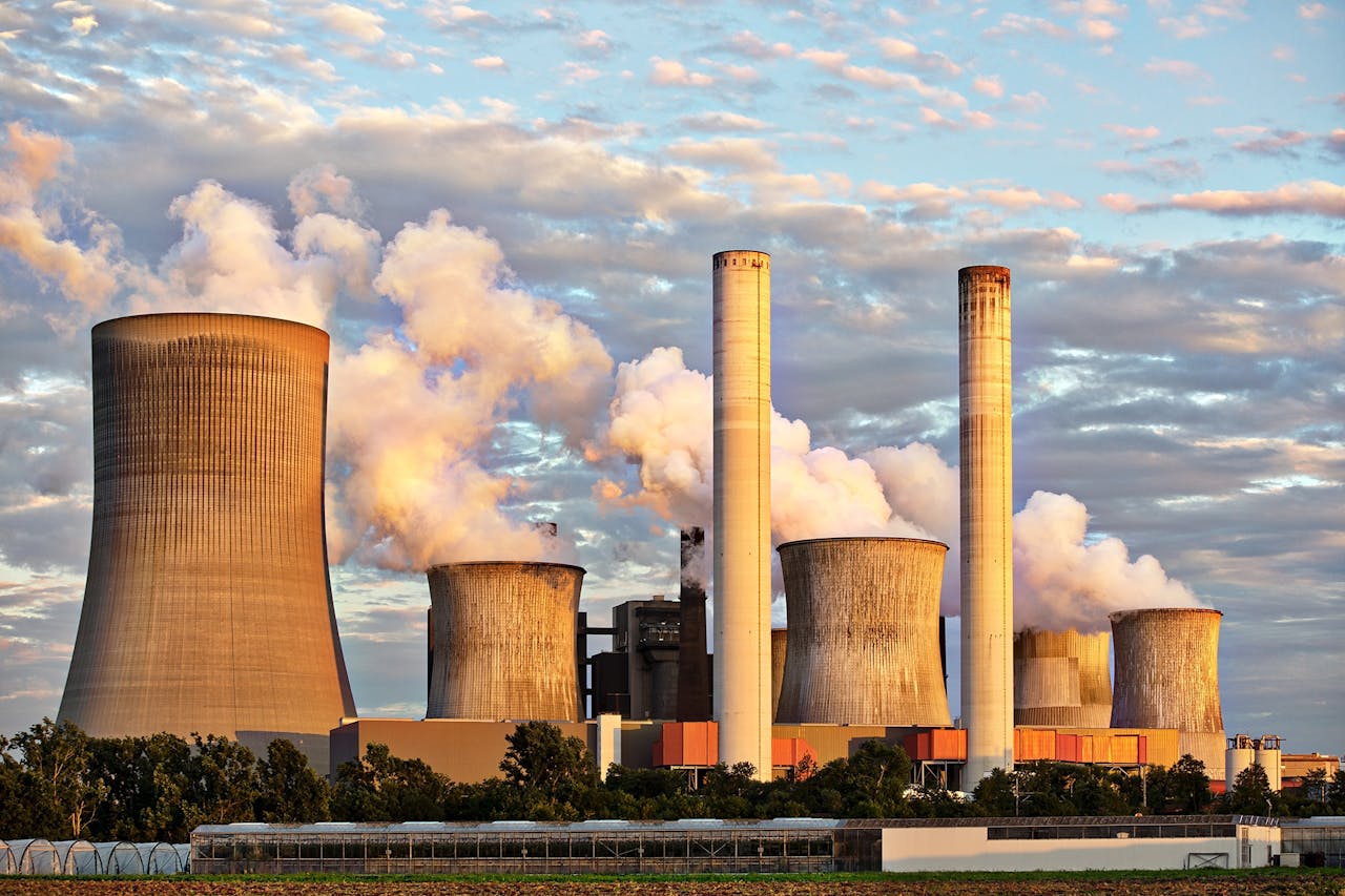 why-choose-us View of a power plant with smoke emissions under a cloudy sky, depicting industrial energy production.